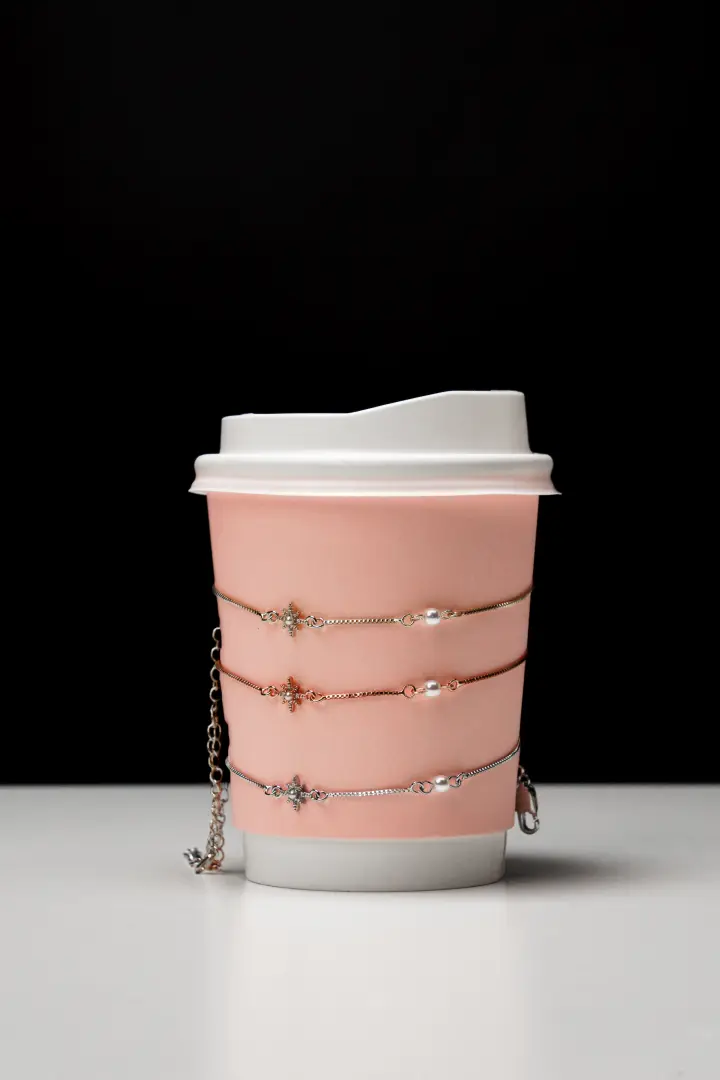 แก้วกาแฟกระดาษสีชมพูซ้อนกันเป็นเสาบนพื้นดำ